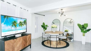 Un espace repas moderne avec une table ronde, des chaises, un téléviseur posé sur un meuble et de grands miroirs sur le mur.