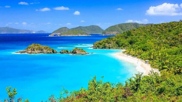 Un paysage côtier caractérisé par une eau turquoise cristalline, une plage de sable et des collines verdoyantes.
