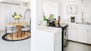 Une cuisine moderne avec des meubles blancs, une cuisinière noire et une machine à café. On y trouve un coin repas avec une table ronde et des chaises, ainsi qu'un vase rempli de fleurs.