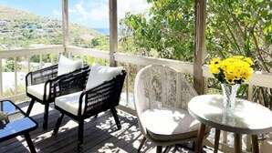A covered outdoor seating area with wicker furniture and a table with yellow flowers. - Oceanview Cottage | Walk to Beach & Restaurants (Cruz Bay)