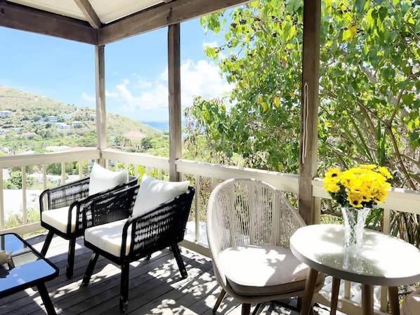 A covered outdoor seating area with wicker furniture and a table with yellow flowers.