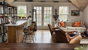 A spacious loft with a high ceiling, a kitchen area with a bar, a seating area with a sofa and chairs, and large windows providing natural light. - Prime cliff road location, Walk to town,  great light, duplex home,  (Nantucket)