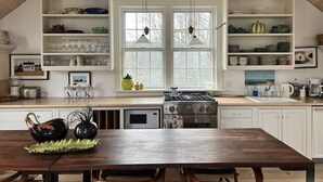 A kitchen with white cabinetry, a wooden table, and a large window with pendant lights. - Prime cliff road location, Walk to town,  great light, duplex home,  (Nantucket)