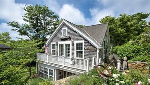 A two-story house with a balcony, surrounded by lush greenery and a stone wall. - Prime cliff road location, Walk to town,  great light, duplex home,  (Nantucket)