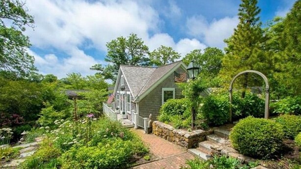 A quaint, single-story house with a stone pathway leading to the front door, surrounded by lush greenery and a clear blue sky. - Prime cliff road location, Walk to town,  great light, duplex home,  (Nantucket)