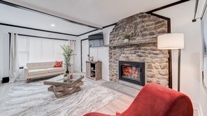 Ein modernes Wohnzimmer mit Kamin aus Stein, einem roten Sessel, einem Holztisch und einem beigefarbenen Sofa.
