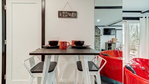 Ein Essbereich mit einem für zwei Personen gedecktem Tisch, einem 'LOVE'-Schild an der Wand und einem roten Stuhl im Hintergrund.