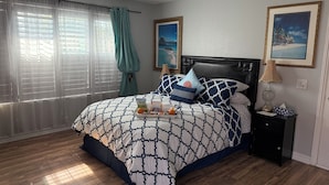 A neatly arranged bedroom with a bed, a bedside table, a nightstand, a chandelier, and a window with curtains. - Romantic Coastal Private Room is located 10 minutes from all sightseeing places  (Oxnard)