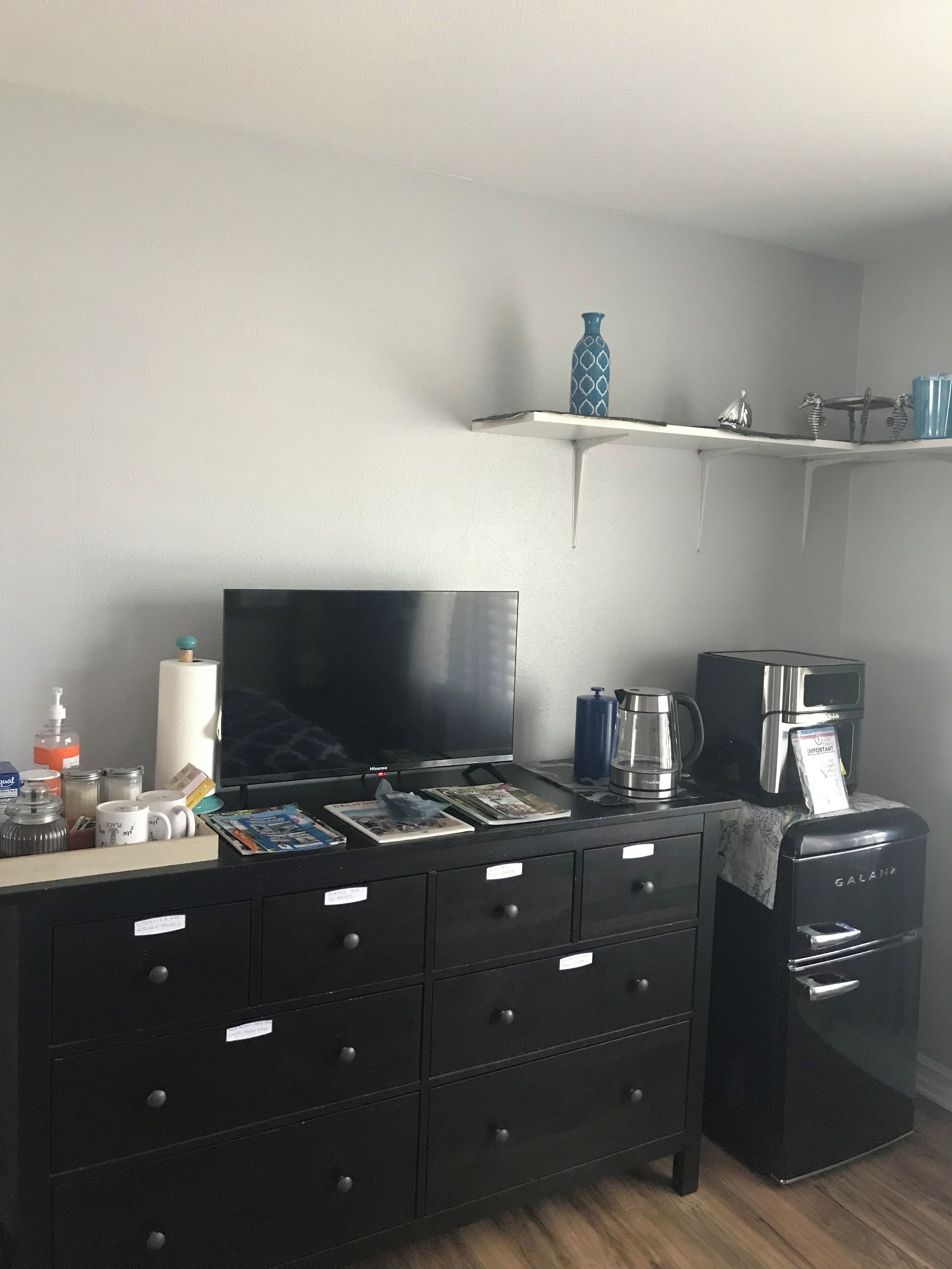 A compact living space with a flat-screen TV, a coffee maker, and a small refrigerator.