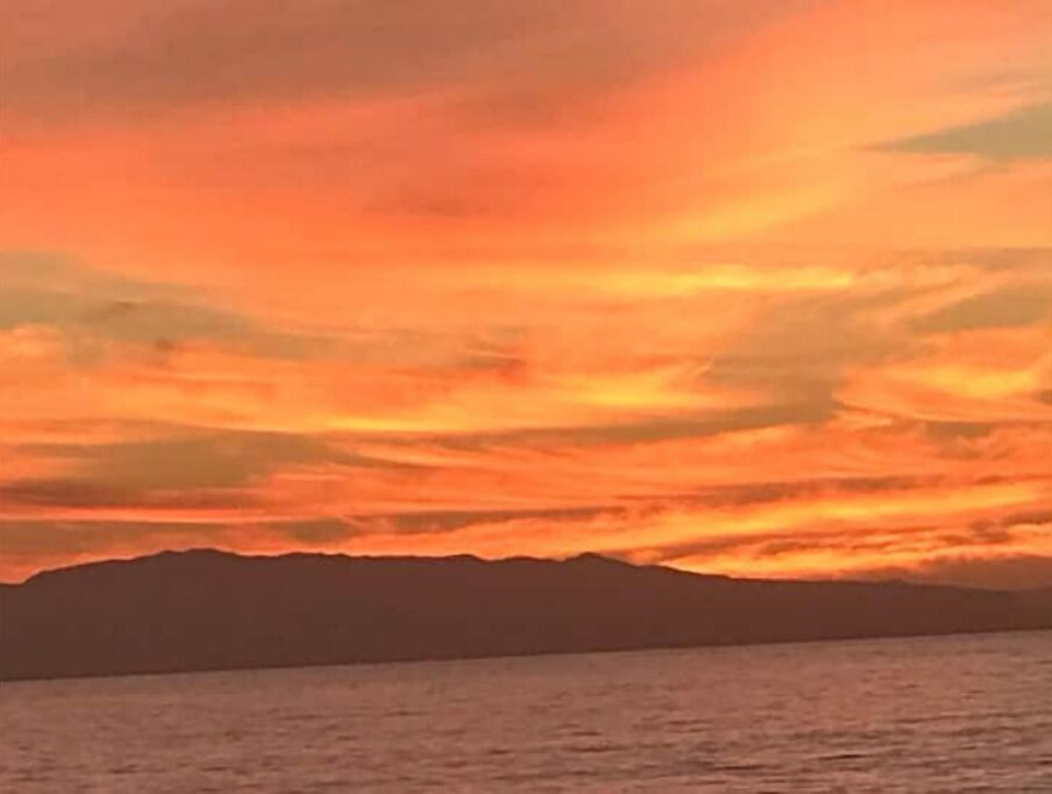 A sunset over a body of water with a mountain range in the background.