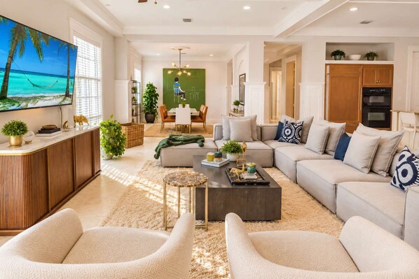 A modern living room with a large flat-screen TV, a dining area, and a kitchen.