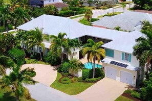 A residential house with a swimming pool, surrounded by palm trees and a well-maintained lawn.