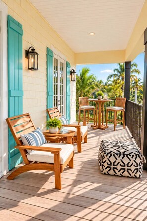 A covered outdoor seating area with wooden furniture and a patterned ottoman. - 505 Sunset Key Estate | Luxury Courtyard Pool Home (Naples)