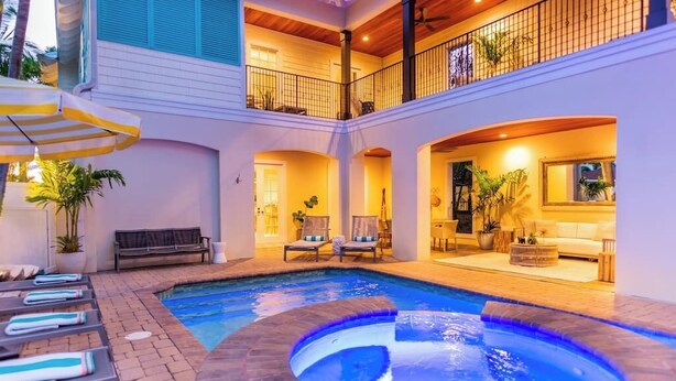 Un área de piscina interior con varios niveles, sillones de descanso, una bañera de hidromasaje y una sala de estar con sofá y mesa.