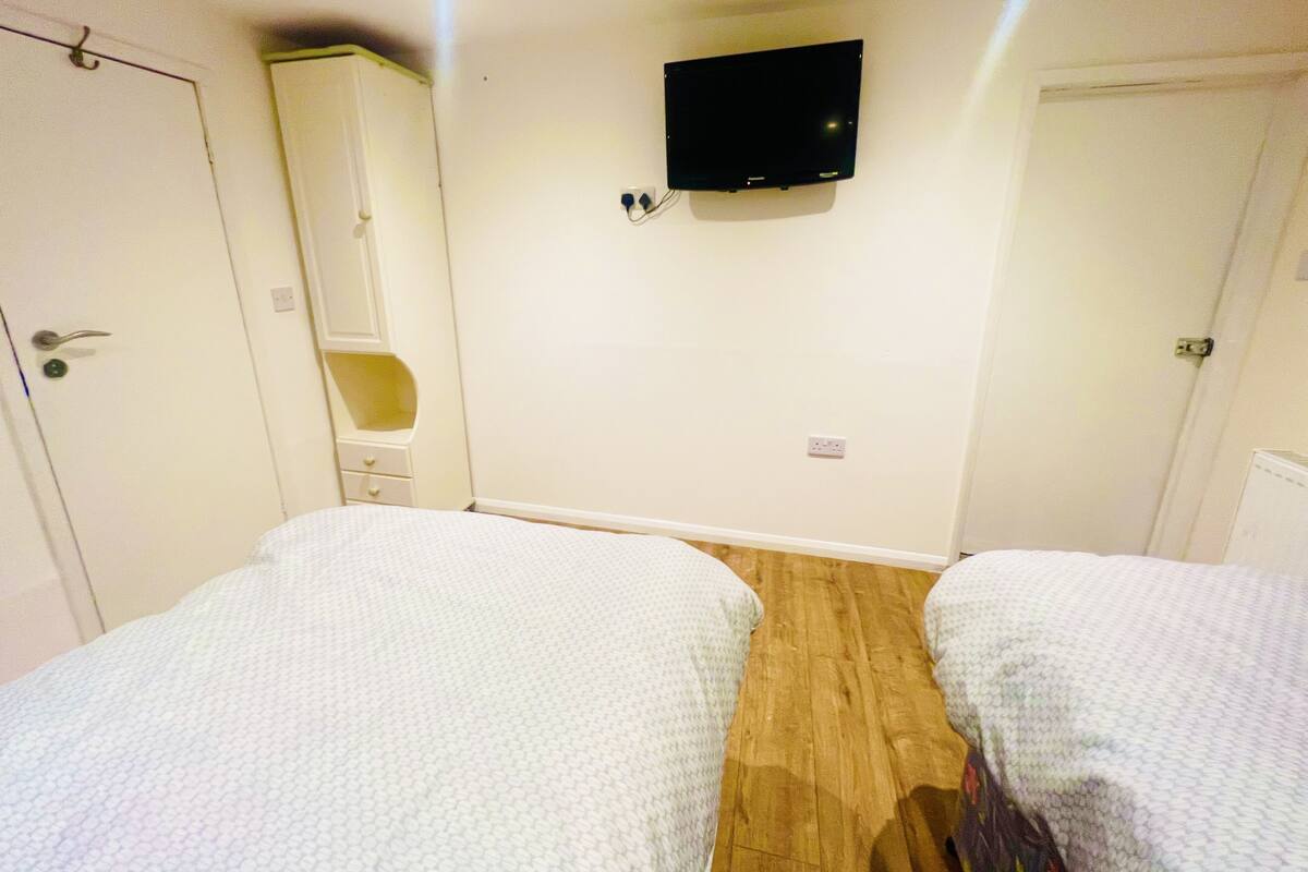 A room with two beds, a TV mounted on the wall, and a wardrobe.