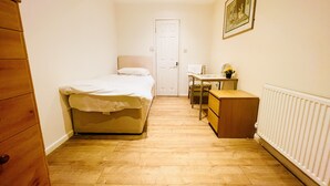 A small, well-lit room with a bed, a desk, a chair, a dresser, and a radiator. - White House Lodge B&B (Cambridge)