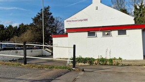 A white building with a red roof, labeled "White House Lodge B&B," featuring a small entrance and a parking area. - White House Lodge B&B (Cambridge)