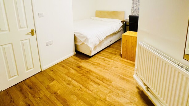 A bedroom with a wooden floor, a bed with a white headboard, a nightstand, and a radiator. - White House Lodge B&B (Cambridge)