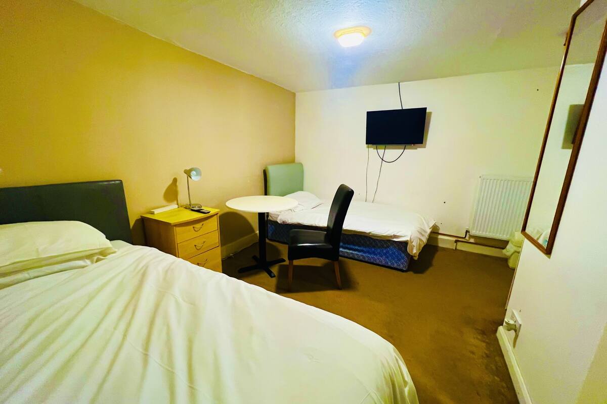A hotel room with a bed, a desk, a chair, a TV, and a radiator.