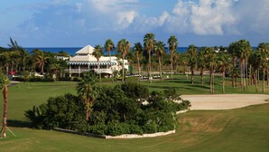 Un campo de golf con un club de campo, palmeras y vistas al océano.