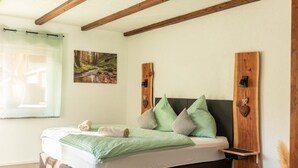 A bedroom with a bed, pillows, a bedside table, a wall-mounted lamp, and a window with a curtain. - Neue, Gemütliche Ferienwohnung mit Großer Terrasse (Wildflecken)