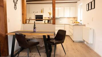 Une cuisine moderne avec des meubles blancs, une table à manger en bois et deux chaises.