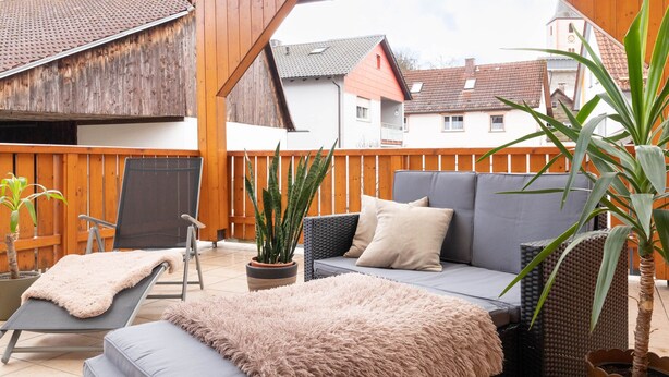 A covered patio with a wicker sofa, a cushioned bench, and a potted plant. - Neue, Gemütliche Ferienwohnung mit Gro ßer Terrasse (Wildflecken)