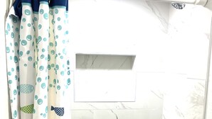 Un angolo doccia con piastrelle di marmo bianco e una tenda da doccia con motivi di pesci colorati.