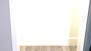 Una stanza con pavimento in legno, parete bianca e un armadio parzialmente visibile con porta.