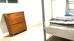 Una camera da letto con una cassettiera in legno, un letto con coperta a righe e una finestra che lascia entrare luce naturale.