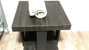 Un tavolo in legno scuro con un asciugamano bianco arrotolato sopra, su un pavimento anch'esso in legno chiaro.