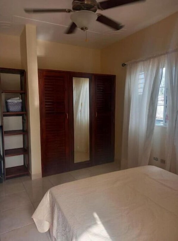 A bedroom with a bed, a ceiling fan, a wardrobe, and a window with curtains.