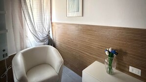 Een kamer met een stoel, een vaas met bloemen, een lijst met een afbeelding en een houten paneelwand.