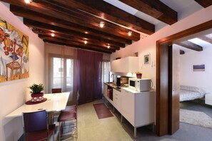 Une cuisine compacte avec un coin repas, un four à micro-ondes et un petit réfrigérateur. Une plante en pot est posée sur la table du coin repas.