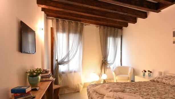Een slaapkamer met een bed, nachtkastje, stoel en een raam met gordijnen.
