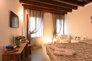 A bedroom with a bed, bedside table, chair, and a window with curtains. - Corte Coppo Deluxe (Venice)