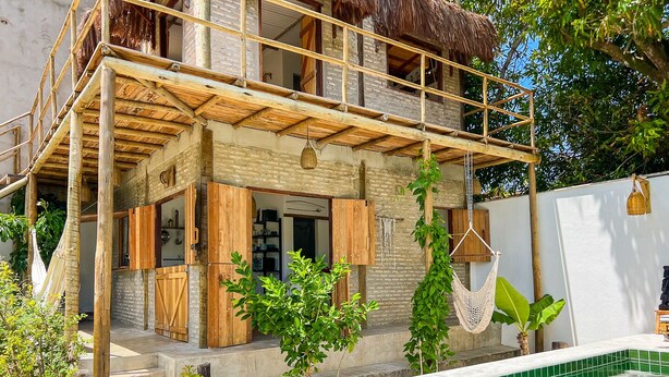 A two-story building with a pool, wooden balcony, and thatched roof.