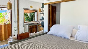 A modern bedroom with a large bed, a wooden desk, and a view of greenery outside.
