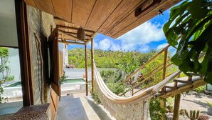 A wooden structure with a hammock, a concrete pathway, and a view of a lush garden and distant hills.