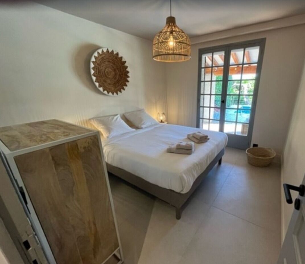 Een slaapkamer met een bed, een hanglamp, een decoratief wandobject en uitzicht door een deur.
