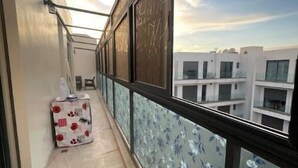 Un balcon étroit doté d’un sol carrelé, d’une cloison en verre ornée de motifs floraux et d’une valise posée sur le sol.