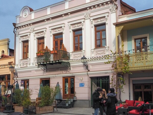 A pink building with ornate architectural details, a balcony with plants, and a sign indicating a restaurant.