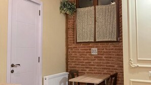 Une pièce avec une porte blanche, un radiateur, un mur en briques, une fenêtre avec des rideaux et une table avec des chaises.