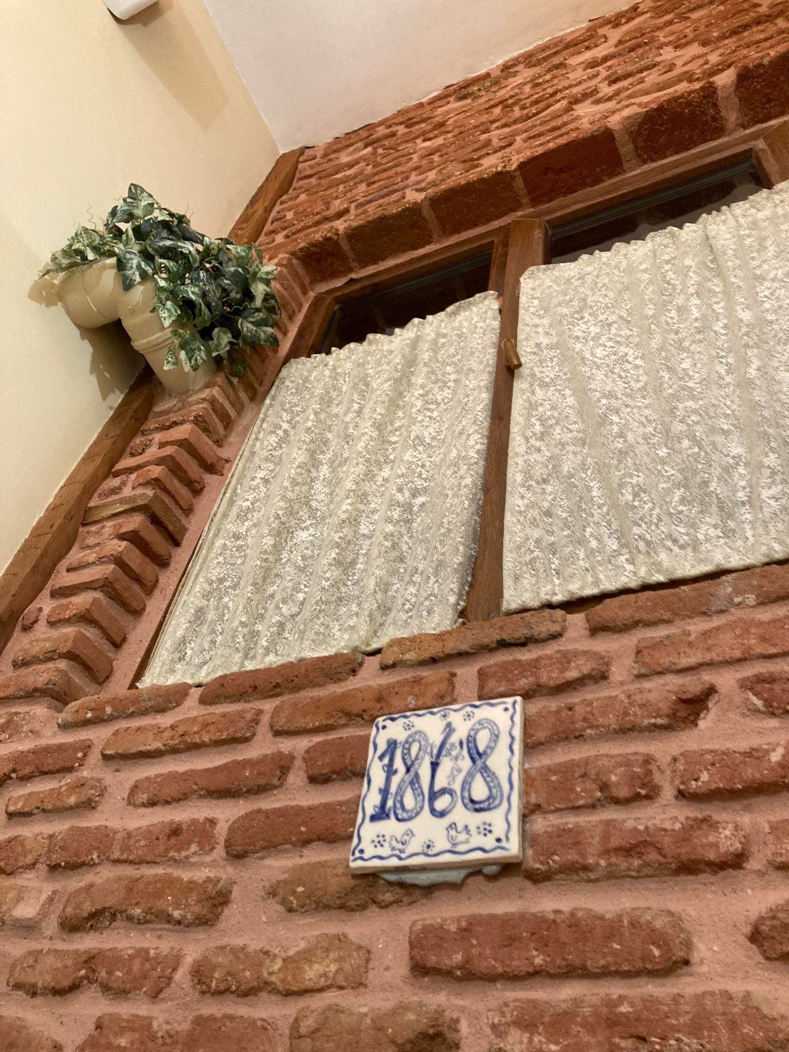 A brick wall with a window and a potted plant. A sign with the number 1868 is visible.