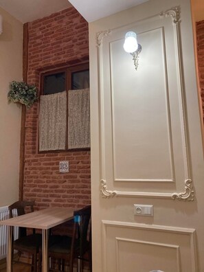A room with a brick wall, a white door with decorative moldings, a window with lace curtains, and a small plant. - Remodeled Deluxe Studio in Historical Building Tbilisi Centre (T'bilisi)