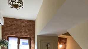 Une chambre à coucher avec un lit, un bureau et une chaise. Il y a un mur en briques et une porte au-dessus de laquelle se trouve un luminaire.