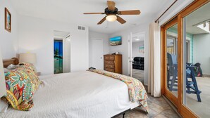 Un dormitorio con cama, ventilador de techo, cómoda y puerta corrediza de vidrio que da a un espacio exterior.