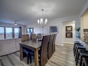A dining area with a large table, chairs, a chandelier, and a television in the background. - La Mirage Condo 235 Beachfront Resort Condominiums (Port Aransas)