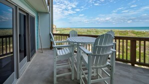 A balcony with a table and chairs, overlooking a beach and ocean.