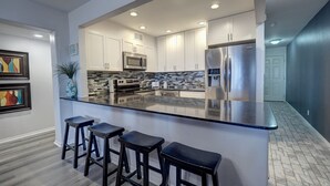 A modern kitchen with white cabinets, a stainless steel refrigerator, a built-in microwave, and a granite countertop.